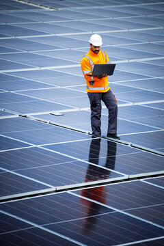 Solar Panels Installation For Sustainable Energy. Electrical Engineer Holding Laptop Computer With Solar Panels Scheme And Checking Productivity.