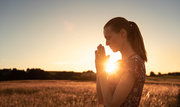 Young woman praying outdoors in the morning light. Religious worship, and spiritual enlightenment concept. 	