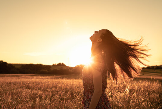 Gorgeous young woman in a wheat field on a sunset background. A fashionable girl with long hair rejoices, laughs, smiles looking up to the sky, enjoys life and summer, nature, happiness. 