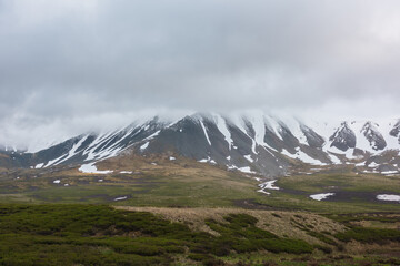 Dramatic alpine landscape with snowy mountains in gray low clouds. Bleak atmospheric scenery of...