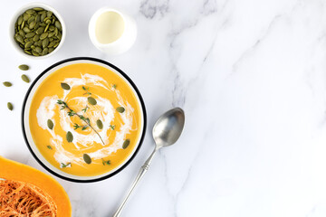 Pumpkin soup with carrots, pumpkin seeds and fresh thyme on a white marble background. Copy space, top view. Food background.