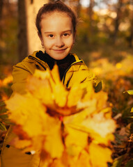 Cute girl with a bouquet of yellow leaves on a walk in the autumn park smiling and looking at camera