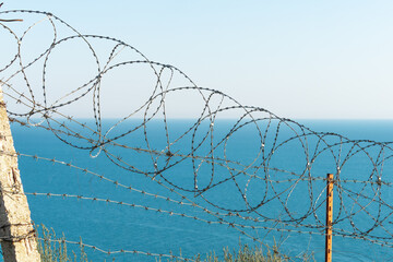 Barbed wire fence on the background of the blue sea. Closed military territory. Access is denied