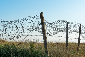 Barbed wire fence against a blue sky and a hilly grassy area. Closed military area