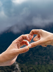 Two hands touching each other making the shape of the heart with a mountainous and cloudy background where only the hands are illuminated