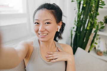 Asian woman blogger filming herself and smiling with headphones, freelance work from home, recording sports workout lifestyle