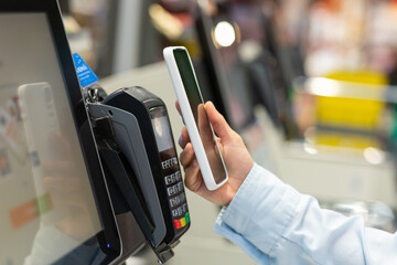 Closeup Woman Counter Buy electronic payment supermarket smartphone Female hand with a mobile phone in pay for purchases in stores Contactless NFC Terminal Closeup card reader.