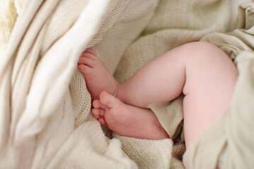 The baby is lying in the crib. The legs of a newborn baby on a knitted blanket.
