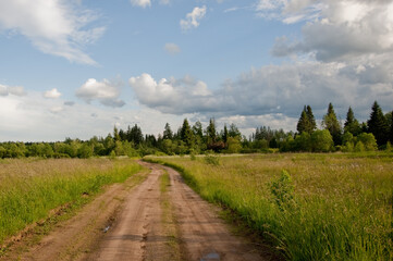 Beautiful sunset. Dirt road through the field. Clouds in the sky.