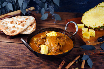 Traditional spicy Indian chicken Madras curry Rogan Josh with drumsticks, wings and pineapple served as close-up in a korei bowl