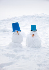 Pair of snowman gentlemen in blue bucket hats. Happy New year and Merry Christmas holiday atmosphere. Winter game play dolls. Xmas party. Copy space. White frozen background. Snowy weather