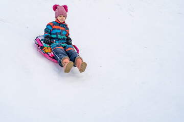Fototapeta na wymiar Little girl sliding downhill on tube. Child sledding in winter hill.