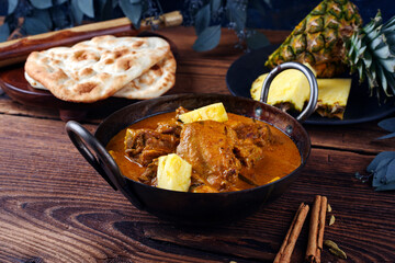 Traditional spicy Indian chicken Madras curry Rogan Josh with drumsticks, wings and pineapple served as close-up in a korei bowl