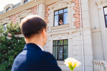 the groom with a bouquet of flowers is waiting for the bride on the window.