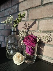 dried flowers stand in a vase in the form of a skull against a brick wall