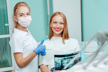 Doctor dentist and woman patient holding x-ray foto with teeth in stomatology clinic with medical equipment. Smile healthy teeth concept