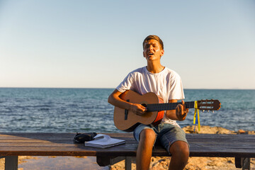 A young stylish guy plays the guitar on the embankment by the sea, the concept of music and relaxation