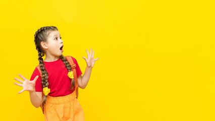A schoolgirl with a satchel looks at your advertisement for educational courses for schoolchildren. A little girl is preparing for exams on a yellow isolated background. Copy space.