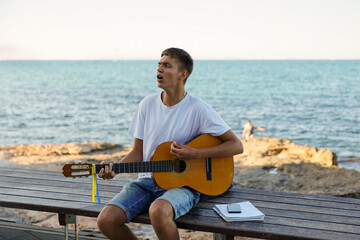 A young stylish guy plays the guitar on the embankment by the sea, the concept of music and relaxation