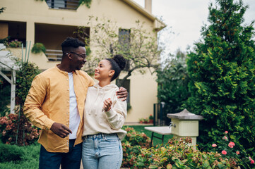 Multiracial couple holding keys and standing outside their new home - obrazy, fototapety, plakaty