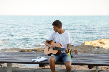 A young stylish guy plays the guitar on the embankment by the sea, the concept of music and...