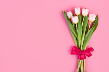 Flatlay beautiful bouquet of white tulips tied with a red ribbon isolated on a pastel pink background with copyspace. object for decoration for women's day, mother's day, anniversary. Spring concept