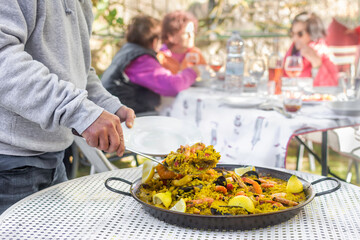 Serving delicious paella at a gathering of friends outdoors. Traditional spanish food. Gastronomy.  