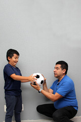 Hispanic dad and son share their love for soccer, they take a ball with their hands excited to...