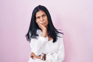 Mature hispanic woman standing over pink background thinking looking tired and bored with depression problems with crossed arms.