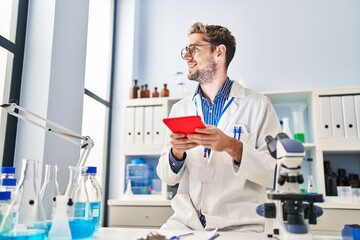 Young man scientist smiling confident using touchpad at laboratory