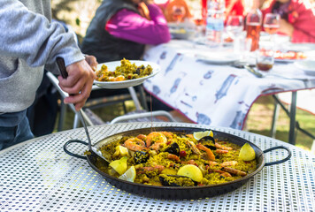 Serving delicious paella at a gathering of friends outdoors. Traditional spanish food. Gastronomy.