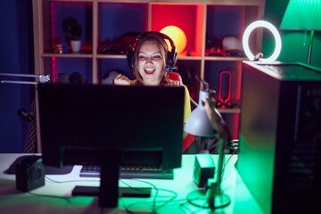 Young blonde woman streamer playing video game with winner expression at gaming room