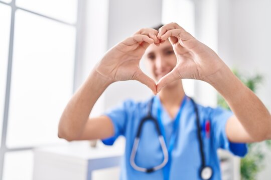 Young beautiful hispanic woman doctor smiling confident doing heart gesture with hands at clinic
