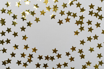 Golden confetti stars on color background, top view