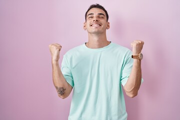 Handsome hispanic man standing over pink background celebrating surprised and amazed for success with arms raised and eyes closed. winner concept.