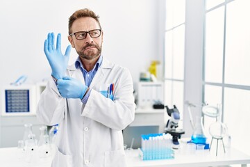 Middle age man working at scientist laboratory smiling looking to the side and staring away thinking.