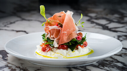 burrata cheese with Italian delicatessen salad with parma ham slices on white plate