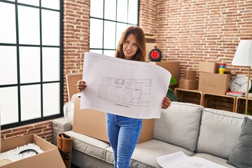 Young latin woman smiling confident holding house plan at hew home