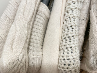 Knitted sweaters and jumpers of beige cream color on hangerts in stack photo from above.