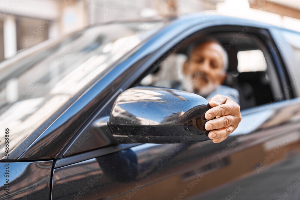 Wall mural senior grey-haired man touching rearview sitting on car at street