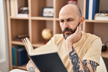 Young bald man reading book sitting on table at home