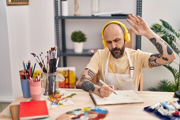 Young bald man artist listening to music drawing on notebook at art studio