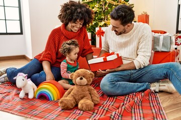 Couple and daughter holding gift sitting by christmas tree at home