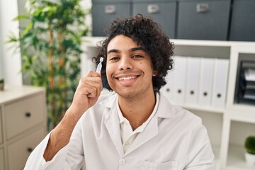 Young hispanic man optician holding eye drop at clinic