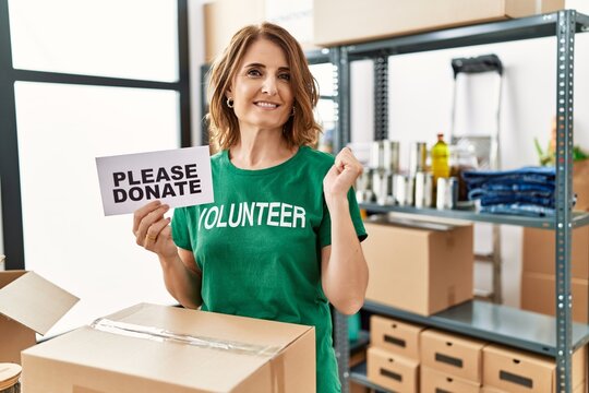 Middle age woman wearing volunteer t shirt holding please donate banner screaming proud, celebrating victory and success very excited with raised arms