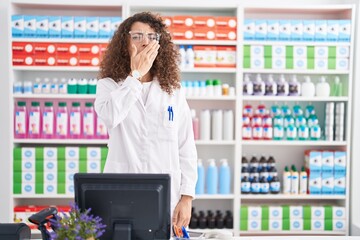 Hispanic woman with curly hair working at pharmacy drugstore bored yawning tired covering mouth...