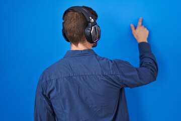 Hispanic man with beard listening to music wearing headphones posing backwards pointing ahead with...