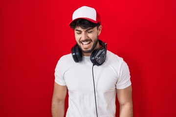 Hispanic man with beard wearing gamer hat and headphones angry and mad screaming frustrated and furious, shouting with anger. rage and aggressive concept.