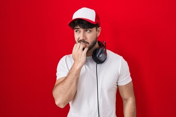 Hispanic man with beard wearing gamer hat and headphones looking stressed and nervous with hands on mouth biting nails. anxiety problem. © Krakenimages.com