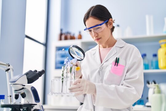 Young woman wearing scientist uniform looking flowers with magnifying glass at laboratory - Powered by Adobe